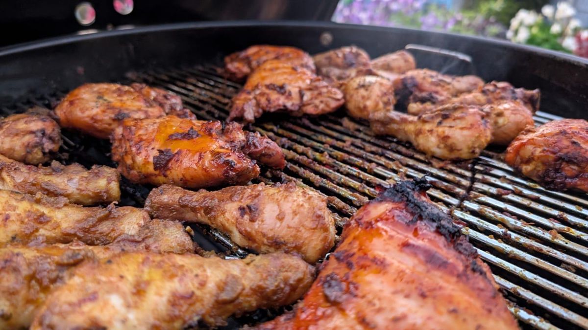 Marinated chicken drumsticks and thighs charring on a kettle BBQ grill
