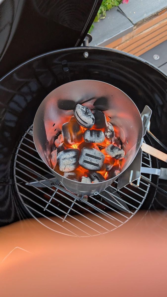 Charcoal briquettes glowing in a chimney starter on a BBQ grate