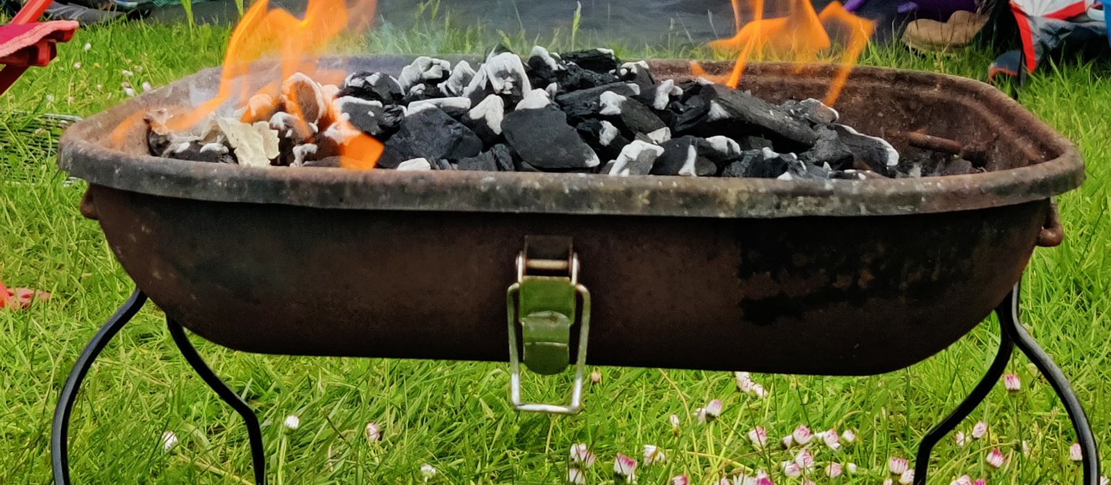 Charcoal catching in a small portable BBQ on grass at a campsite