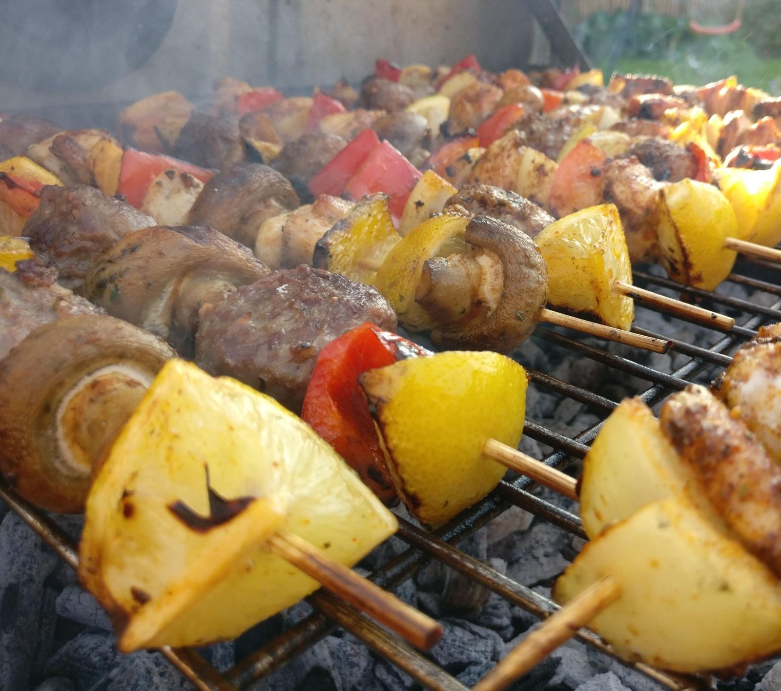 Close-up of skewers with mushrooms, peppers, lemon and chicken on a BBQ