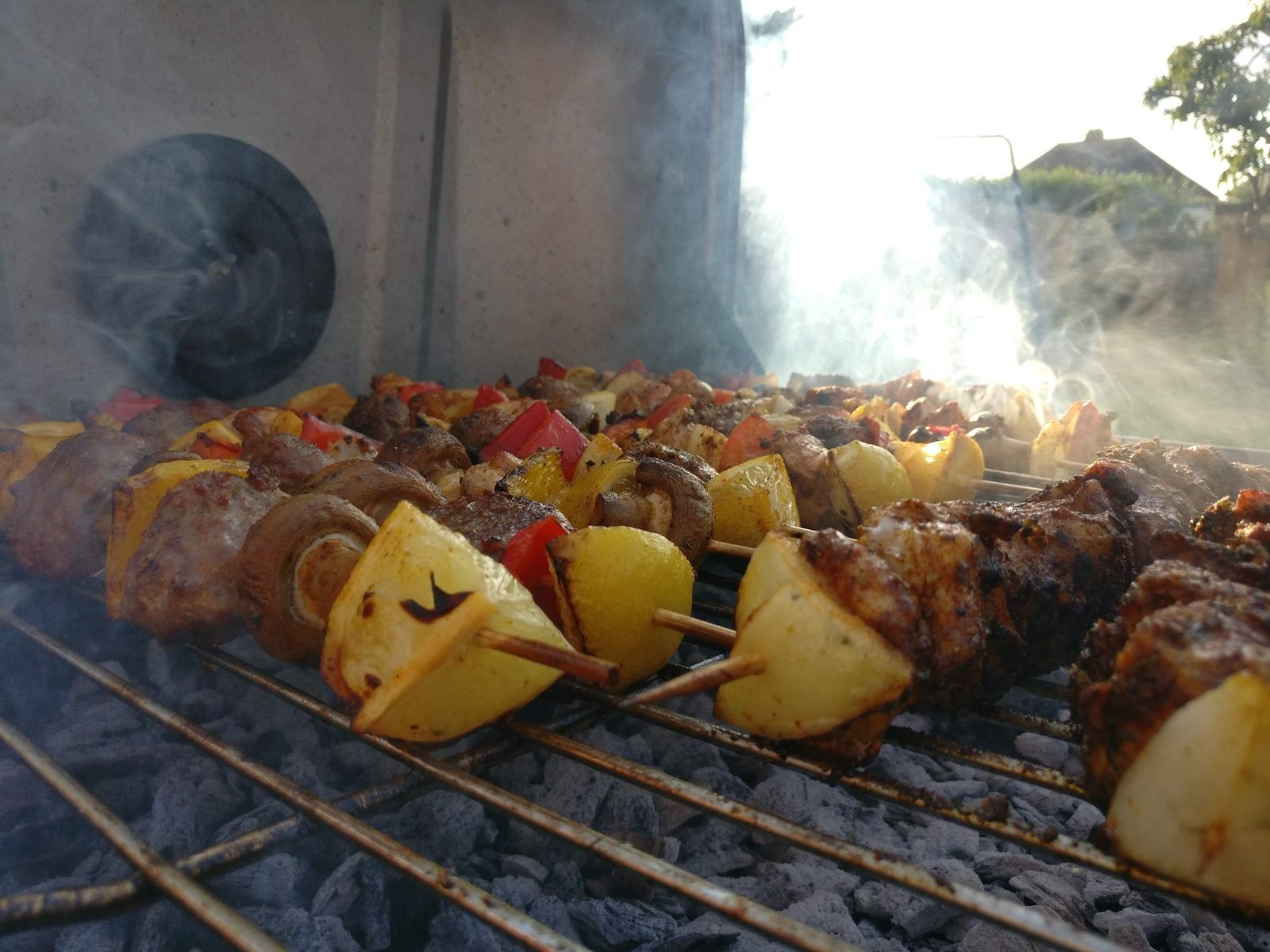 Skewers cooking on a BBQ with smoke drifting in the evening sun