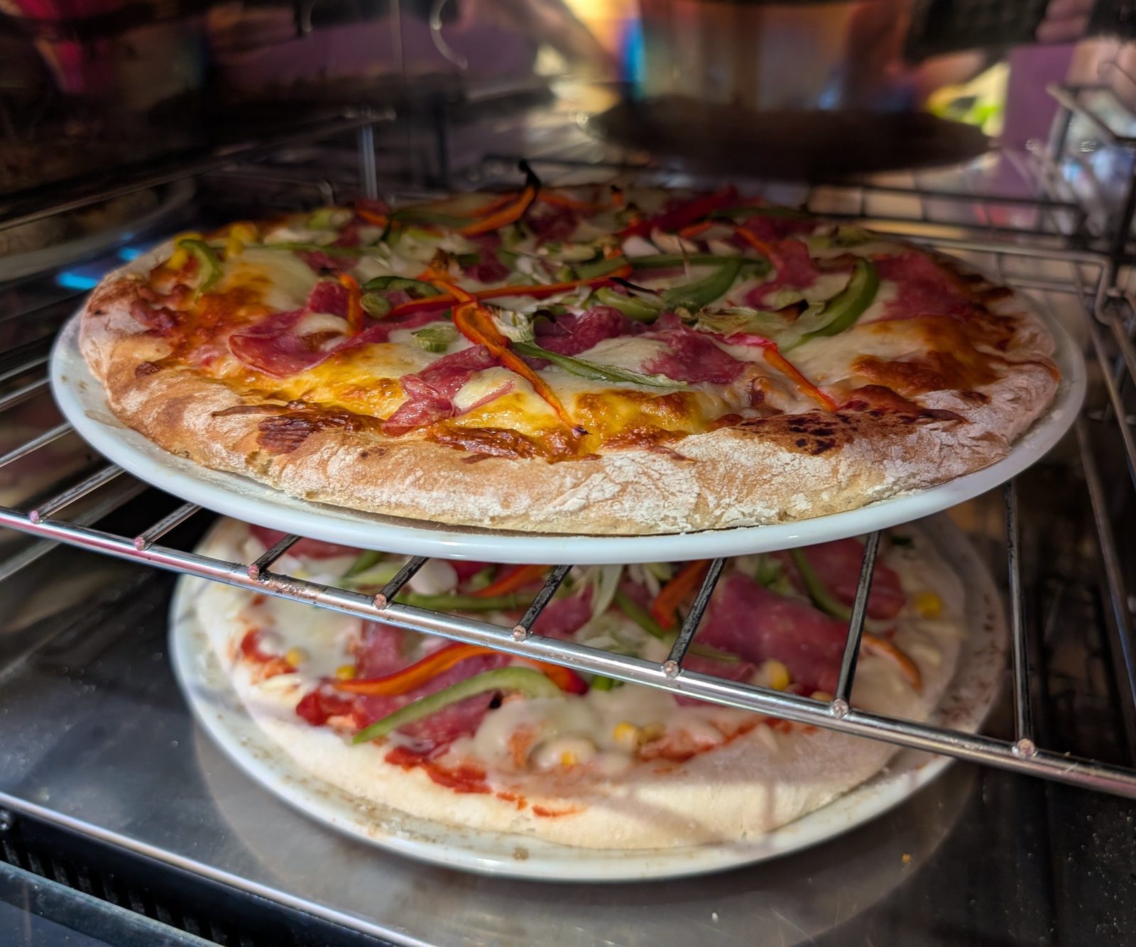 Two homemade pizzas cooking on the shelves of a kitchen oven