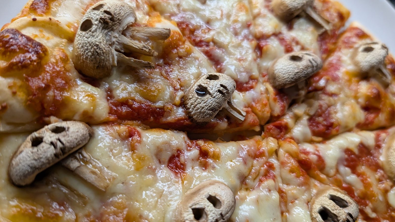 Close-up of mushrooms carved into skulls on a melted cheese pizza