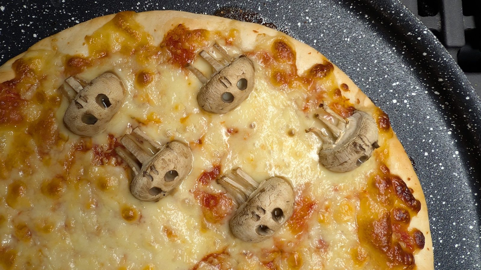 Mushroom skulls on a cheese and tomato pizza in a round pizza tray, fresh from the oven