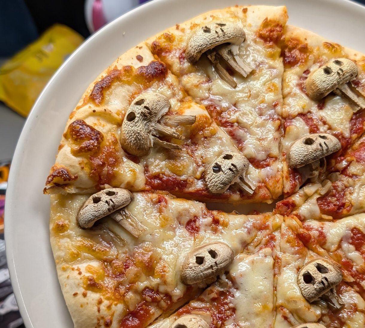 Homemade cheese and tomato pizza decorated with mushrooms carved into skulls for Halloween