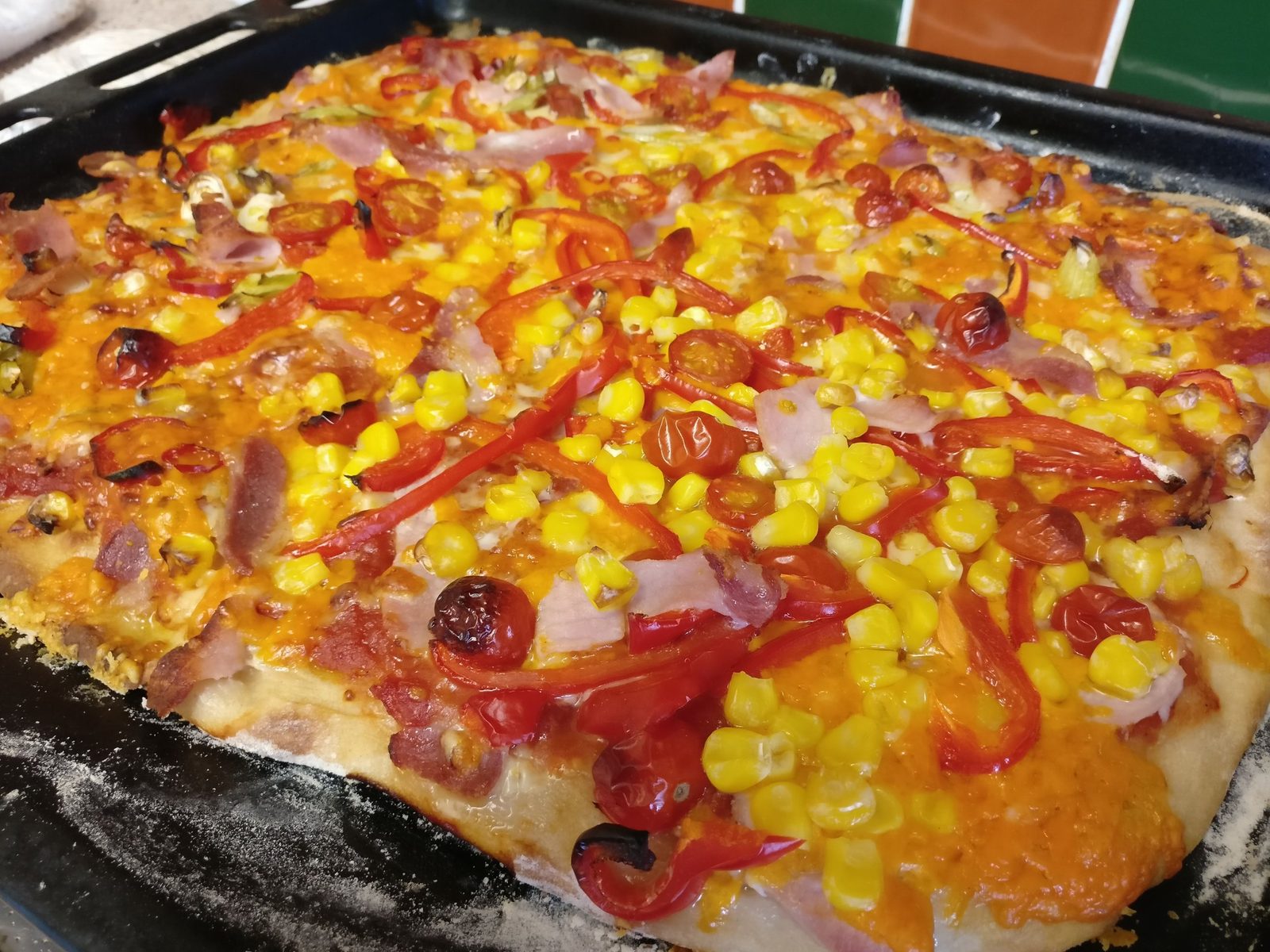 A homemade tray pizza with bacon, sweetcorn, peppers and cherry tomatoes fresh from the oven