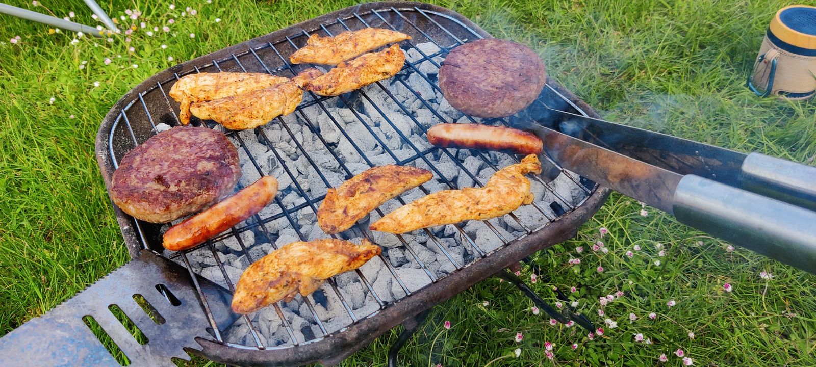 Chicken, burgers and sausages on a small portable charcoal BBQ on grass