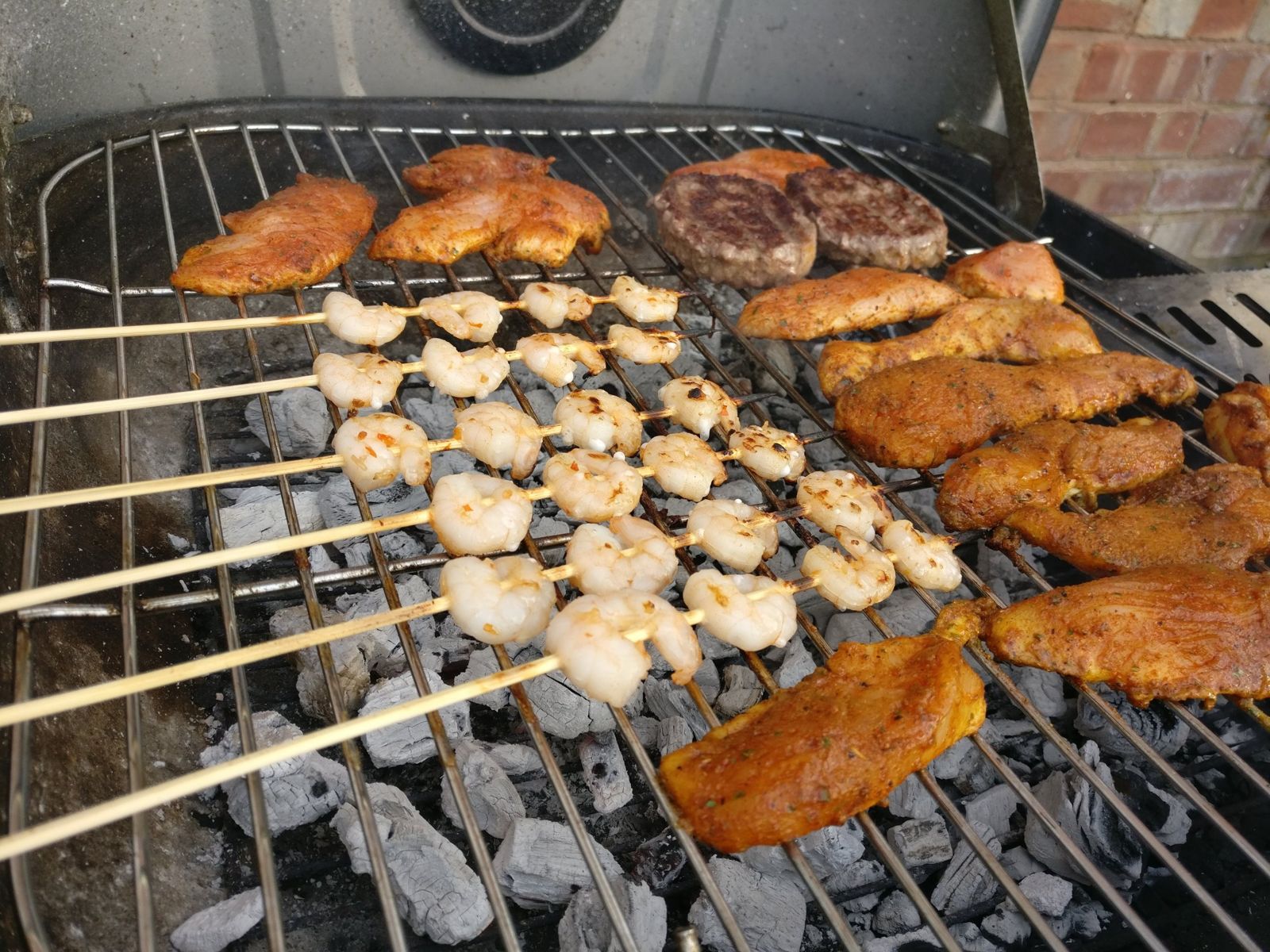 Garlic prawn skewers cooking on a charcoal BBQ next to chicken and burgers