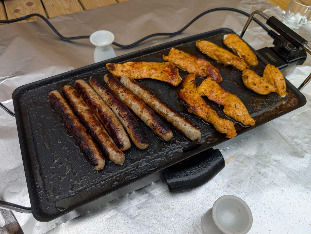 Seasoned chicken strips and sausages cooking on an electric griddle