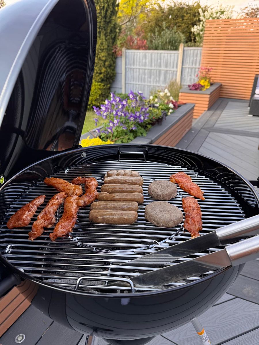 Marinated chicken strips, sausages and burgers just placed on a kettle BBQ