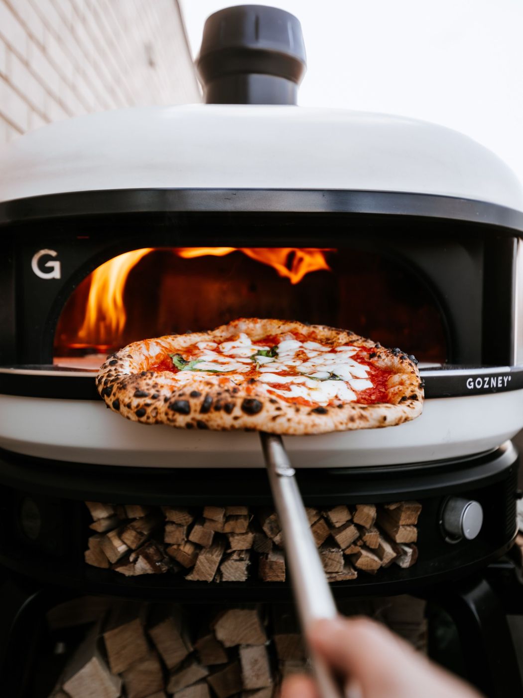 Pizza on a peel in front of a Gozney Dome oven with flames inside