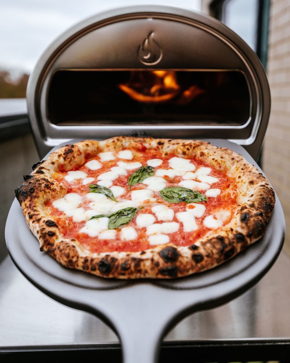 Margherita pizza on a peel in front of a Gozney oven