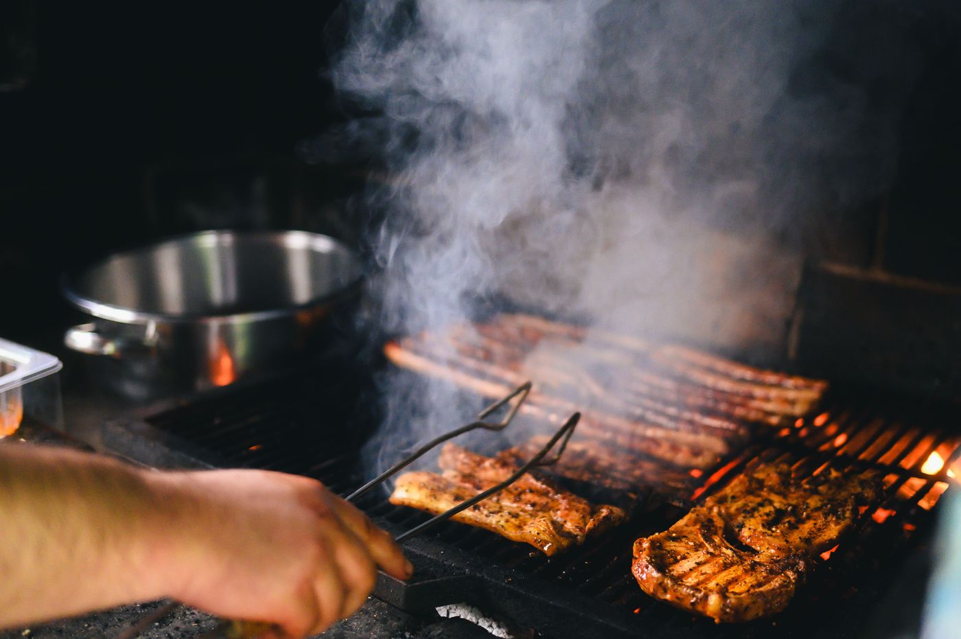 Tongs turning food on a smoky charcoal grill
