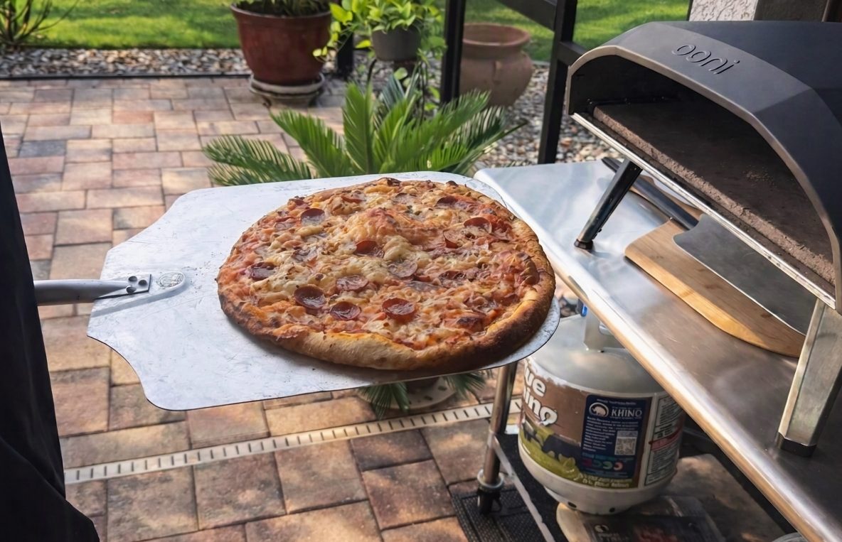 Ooni Koda gas pizza oven on an outdoor prep table with a pizza on a peel