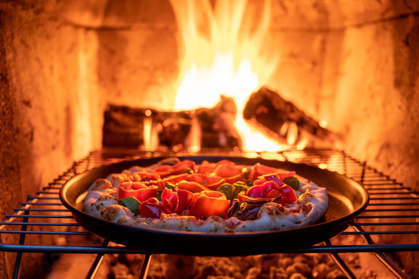 Pizza cooking in a pan on a grate over a wood fire