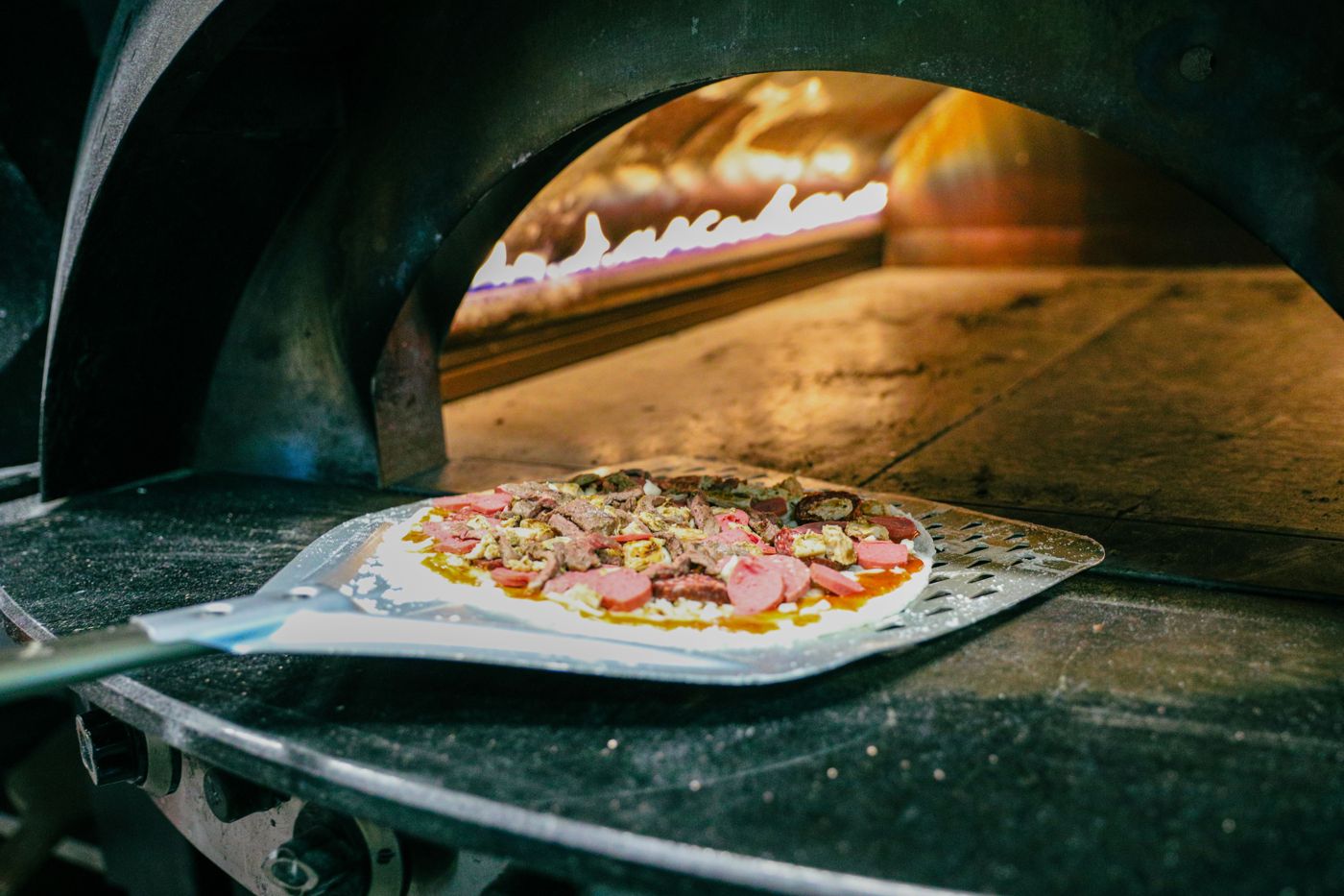 Pizza being slid into a gas pizza oven with a peel