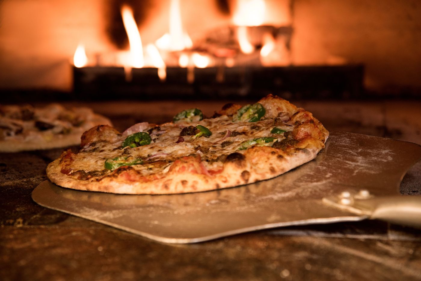 Pizza peel sliding a pizza into a wood-fired oven