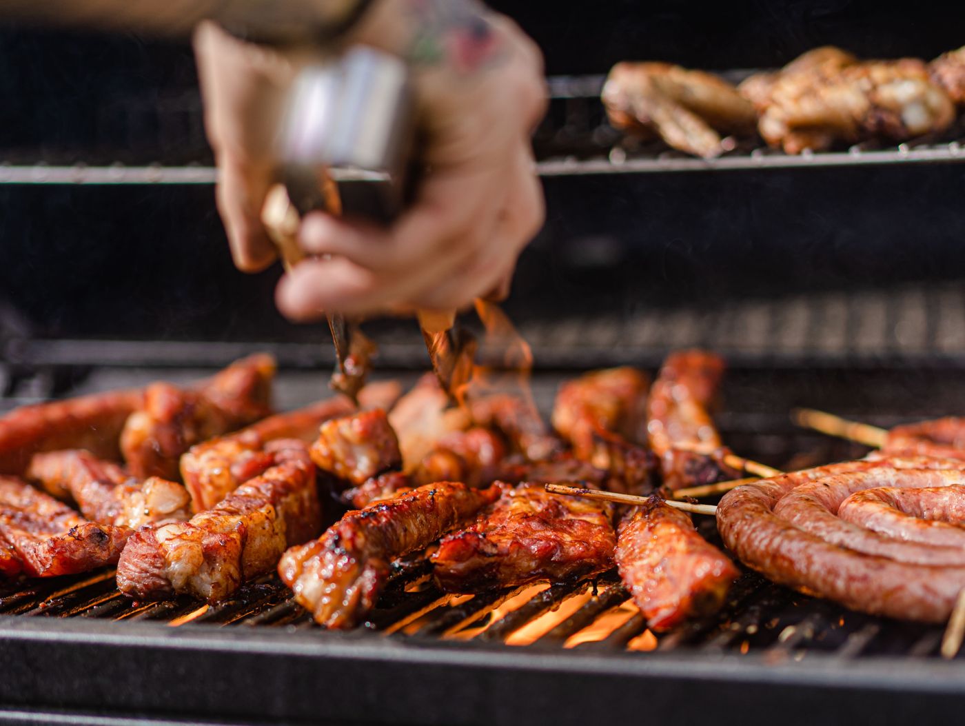 Ribs and sausages being turned with tongs on a grill