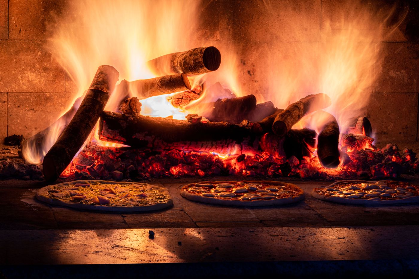 Three pizzas beside a log fire