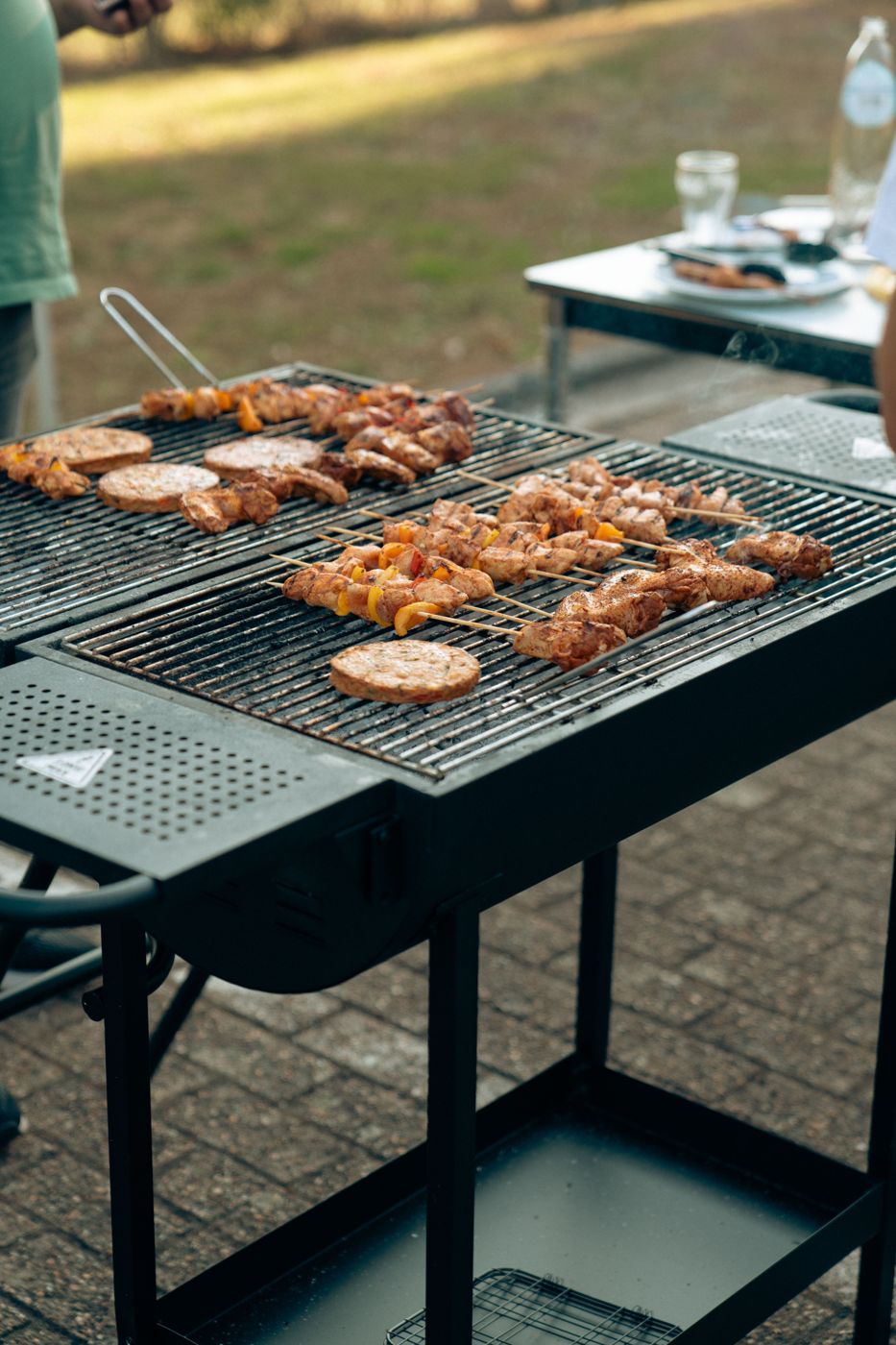 Skewers on a BBQ with a prep trolley alongside