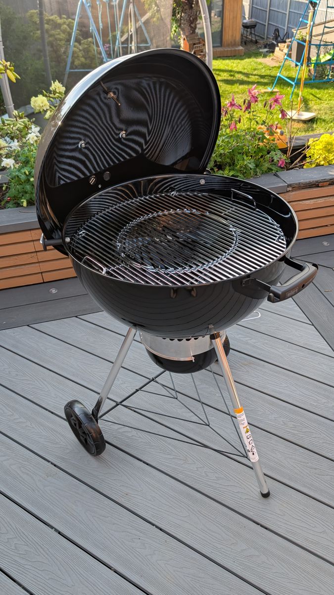 Black Weber Master-Touch kettle BBQ with the lid open on a grey composite deck